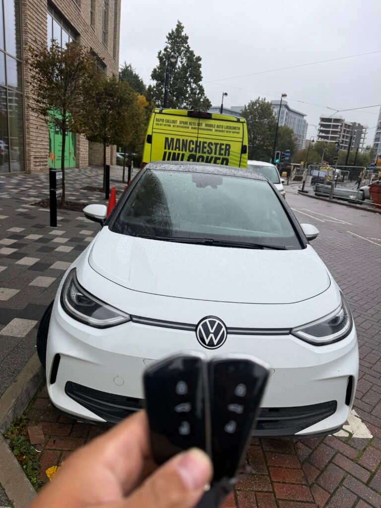 Two keys held in front of a white Volkswagen ID.3 and the Manchester Unlocked van in Salford Quays